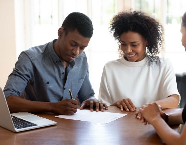 A young man and woman sitting at a table while the man writes on a piece of paper.