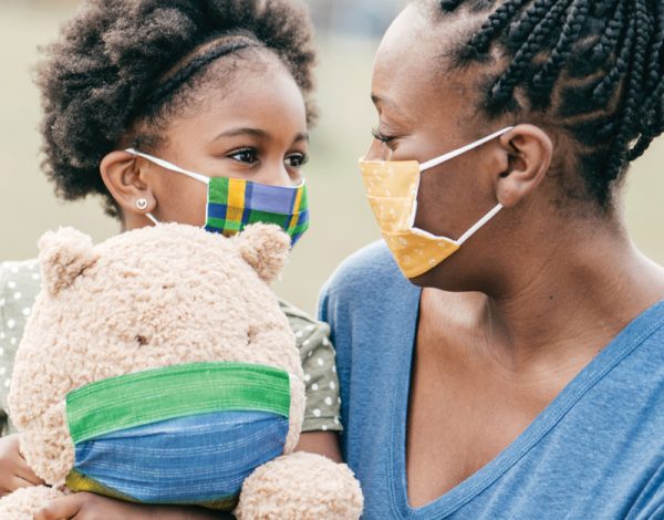 A woman and child, both wearing colorful masks, gaze at each other affectionately.