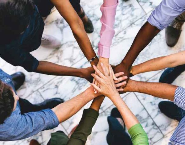 Diverse group of hands joined in a circle over a marble surface, symbolizing unity and teamwork.