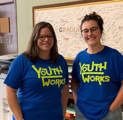 Two people smiling, wearing matching blue "Youth Works" T-shirts.
