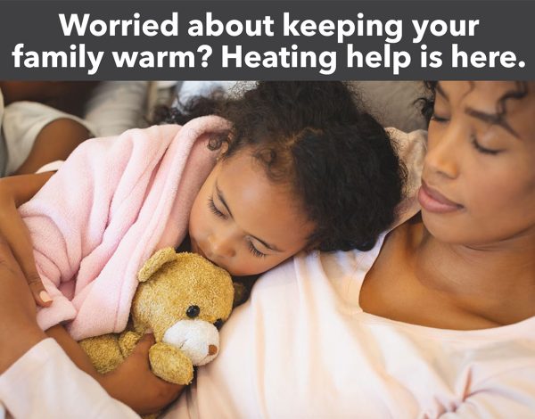 A mother and child cuddle on a couch, wrapped in a pink blanket. The child holds a teddy bear. Text above: "Worried about keeping your family warm? Heating help is here."