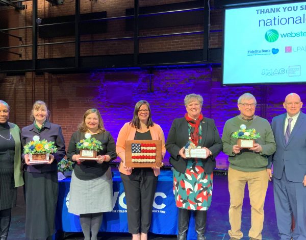 Seven people, six holding awards, stand on a stage with a "Thank You Sponsors" sign above.