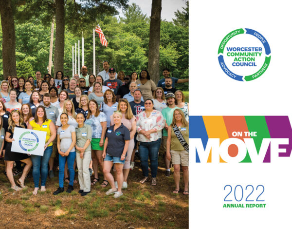 A large group of diverse individuals stands in a wooded park, smiling, with an American flag in the background.