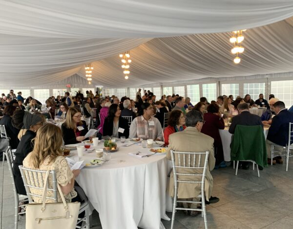 A large group of people seated at round tables in a well-lit, elegantly draped banquet hall.
