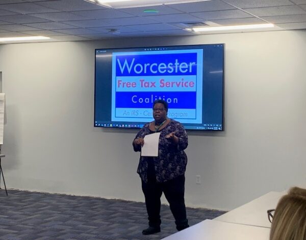 Person presenting in a conference room with a screen displaying "Worcester Free Tax Service Coalition."